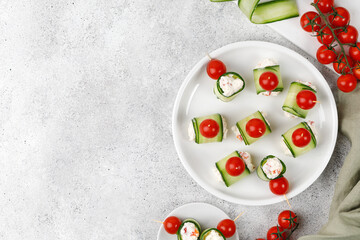 Cucumber rolls stuffed with cream cheese, tomatoes cherry over it, served on a white plate. Holiday vegetable appetizer, snack for a festive table. Mini fresh canapes.