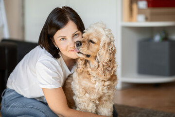 Attractive young brunette hugs her American cocker spaniel dog sitting at home on the floor. the concept of love for pets