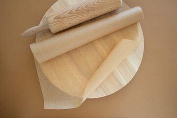 wooden rolling pin, wooden board, baking paper on a brown background