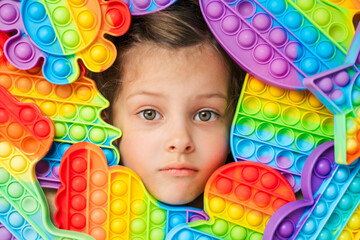 Little girl,kid,child head among many,lots of colorful pop it. Children play. Trendy silicone antistress colorful sensory push toy popit. Flapping fidget. Rainbow color.Cure of autism.Stress reliever