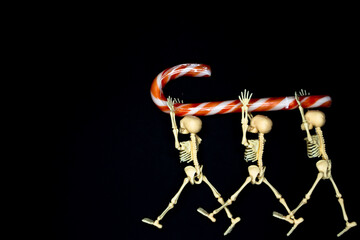 Three skeletons carry a candy cane. Halloween treats. Halloween parties. Day of the Dead.