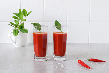 two glasses of tomato juice and chili peppers on the table indoors