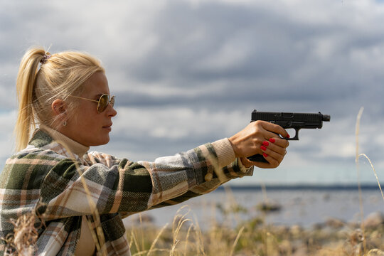 Blonde girl takes aim from a pistol outdoors in a field.