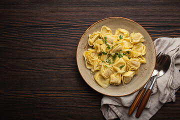 Italian filled tortellini ravioli on ceramic plate top view on dark rustic brown wooden table...