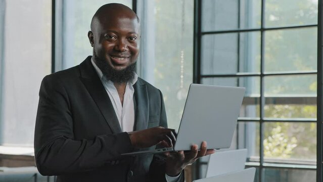 Businessman american african entrepreneur ceo analyst investor stand in modern skyscraper office hold laptop work in marketing department e-commerce online emailing message chatting with colleagues