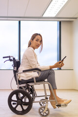 Office workers woman on a wheelchair in bright office and holding smart phone. 