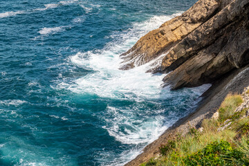 Beautiful Asturias landscape with high cliff, big stones, green grass. Atlantic Ocean with beautiful colours and reflections. Cloudy sky. In background few small islands. 