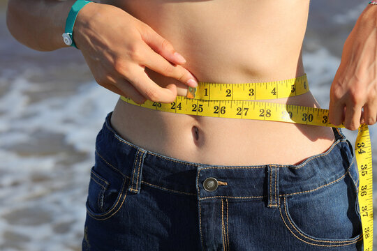 skinny girl measures her waistline after the weight loss diet with a yellow flexible measuring tape