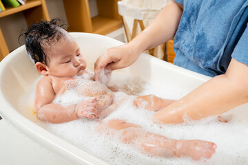 Fototapeta premium Close-up of a newborn baby in Asia lying in the tub. single mother gradually Bathing the newly born daughter And the daughter's face and body were filled with bubbles.