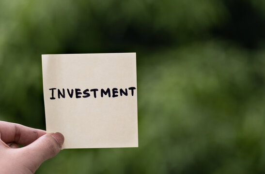 Outdoor image of investment word written on sticky note green dark blurred background.Concept of investment planning written on note pad. People should invest with plan.