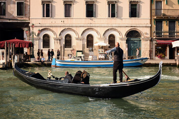 Fototapeta na wymiar October 16, 2019, Venice, Italy: A gondola carrier takes a tourist along the Grand Canal, with a building and vacationers in the background