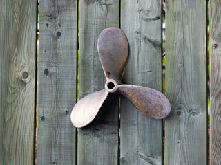 Small old brass three wing boat propeller attached on wooden fence as a decoration 