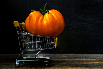 A huge orange tomato with water dew drops in a supermarket cart. The concept of selling natural food. Background old wooden.