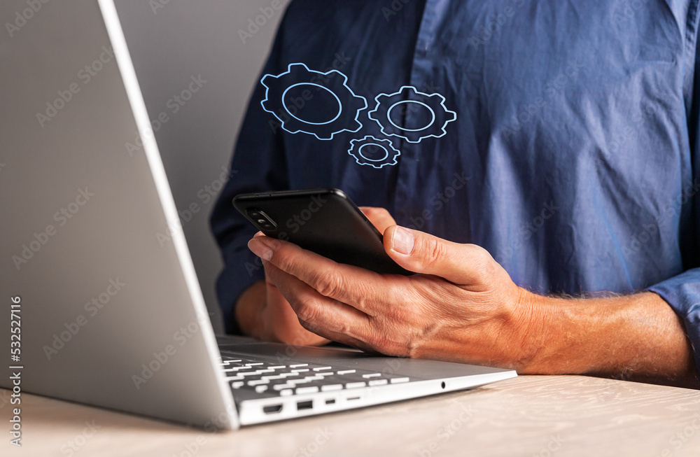 Poster Man holding phone with virtual gears while working on laptop. Mobile settings or strategy, process organization, business idea concept.
