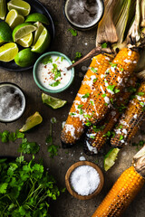 Grilled corn cobs with fresh herbs,lime,beer and salt, served on stone table.