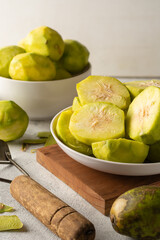 sliced ambarella or june plum on white textured surface, cut and peeled edible fruits in a bowl for making vegetarian condiment or sauce, soft-focus background with copy space