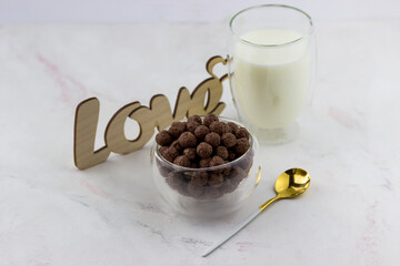 Snacks in the form of chocolate balls. A bowl with a quick breakfast, a glass of milk and the inscription love on a white marble background