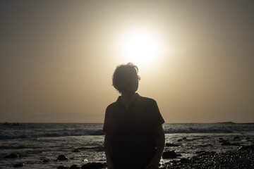 Silhouette of mature caucasian woman walking on the beach at sunset light - horizon over sea