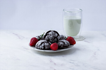 Chocolate cracks cookies on a white marble table. Delicious cookies, a cup of milk and strawberries