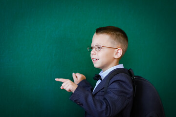 A Happy child child standing at the blackboard with a school backpack wearing glasses