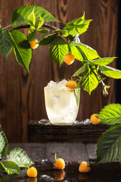 Refreshing drink of yellow raspberry surrounded raw ripe berries and green leaves. Dark wooden background. Backlight