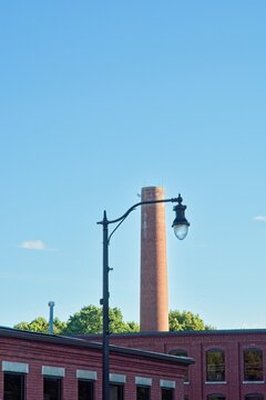 Old mill brick smokestack chimney set behind brick textile mill buildings and street light