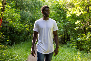 African american man in a white t-shirt walks in a green forest. Mock-up