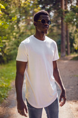 Fototapeta na wymiar African american man in a white t-shirt walks in a green forest. Mock-up