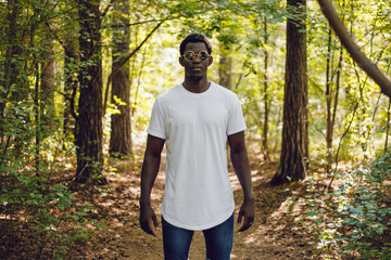 African american man in a white t-shirt walks in a green forest. Mock-up