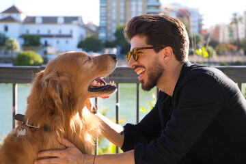 young latino man with sunglasses and beard and his brown golden retriever dog look at each other...