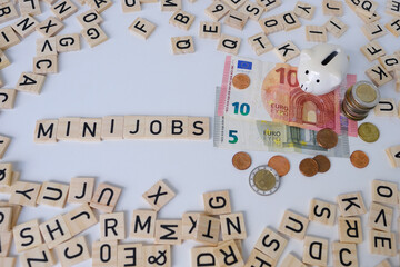paper euro banknotes, piggy bank, bills on table among euro coins, word Mini job with wood blocks,...