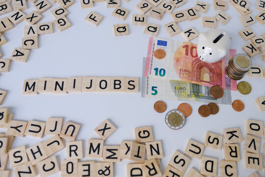 paper euro banknotes, piggy bank, bills on table among euro coins, word Mini job with wood blocks, part-time with low wage concept, marginal employment, help for pension fund, health insurance