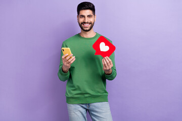 Photo of handsome positive toothy beaming man dressed green pullover hold hand smartphone like...