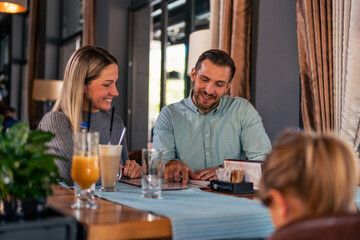 husband and wife with their daughter are looking at the offer of the restaurant where they came for a family lunch
