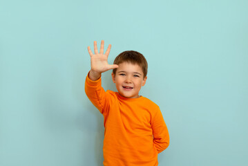 child boy showing five fingers on blue background copy space. portrait of a 5 year old boy