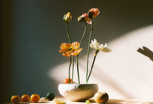 
various poppies and fruits placed in a white vase