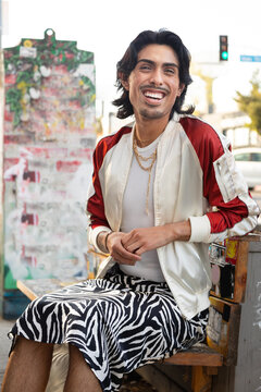 Queer latin person in trendy outfit laughing and sitting on bench