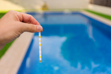 Hand with measuring pool strips to check water quality in a swimming pool