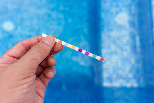 Hand with measuring pool strips to check water quality in a swimming pool