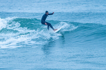 Surfer riding a wave with on a foggy morning in Furadouro beach, Ovar - Portugal.