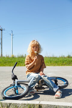 Little bicyclist blowing off seeds from dandelion