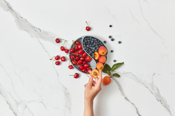 Plate with fruits, female hand taking apricot.