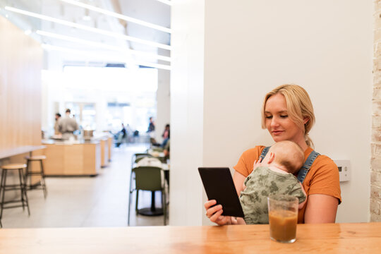 Young Woman Uses An E-Reader While Holding Baby In Arms 