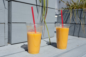 Two plastic cups with mango shake on a city bench, mockups, open space