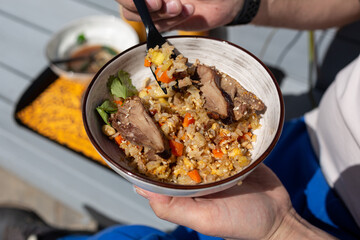 Close-up of a plate in the hands of a man with rice and duck, a young man having lunch with duck and rice in a street cafe in the park