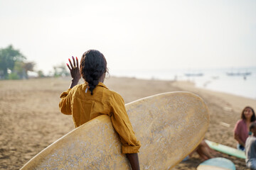 Woman in long sleeved shirt carrying surfboard at beach