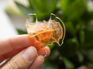 an apparatus for correcting the bite in children, in the hand of a girl, against the background of a houseplant, in daylight. Hygiene, dental treatment, bite correction, new technologies.