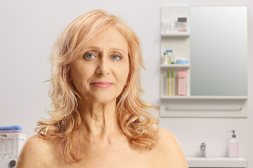 Portrait of a mature woman with blue eyes and bare shoulders in a bathroom