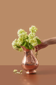 Etched copper vase with blooms held by woman.