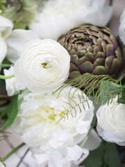 Delicate bouquet in white and green tones. White ranunculus, peonies, green twigs and leaves and a green artichoke in a bouquet.
